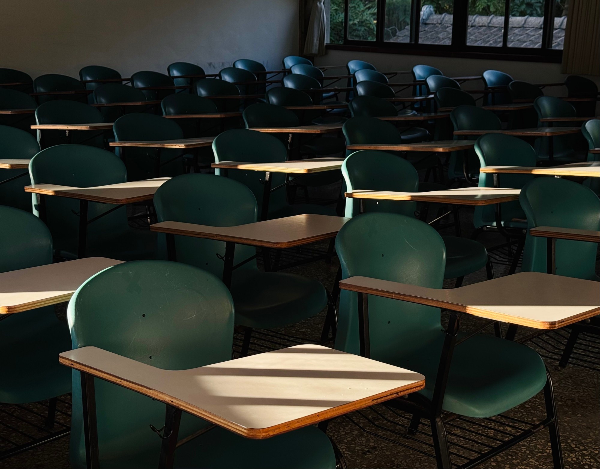 Rows of empty classroom chairs with fold-out writing desks, lit by late afternoon sun